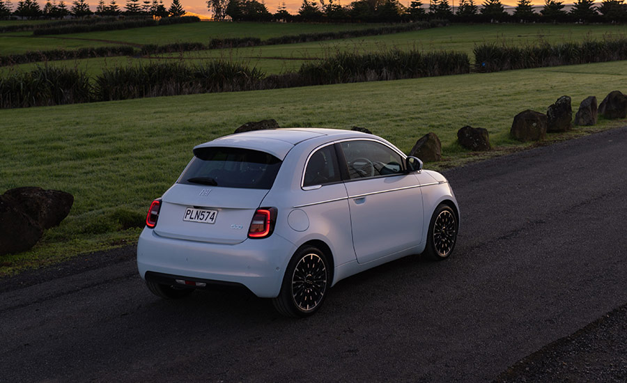 A white Fiat 500e electric car driving on a country road at sunset