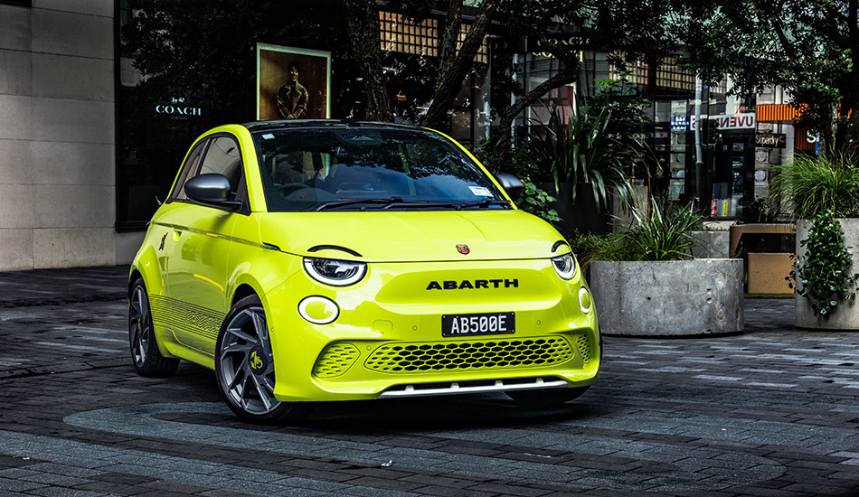 Green Abarth hatch parked next to a garden