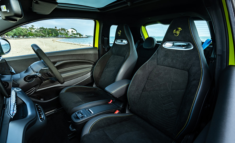 The interior of a yellow Abarth 500e electric car. The car features black sport seats with the iconic Abarth scorpion logo embroidered on the headrests.