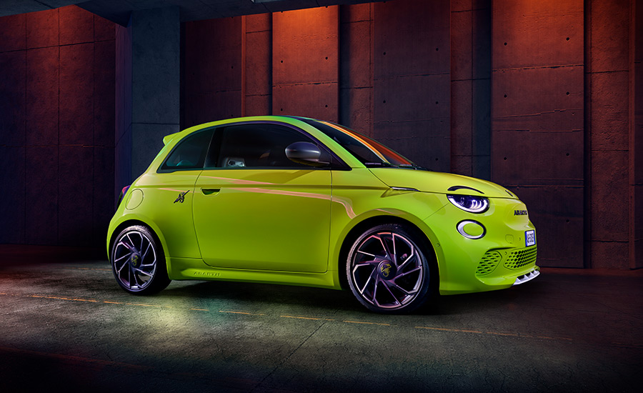 A vibrant green Abarth 500e electric car parked in a dimly lit garage, with dark windows.