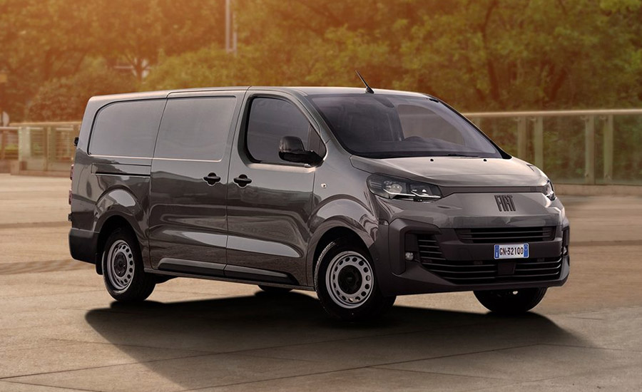 Grey panel van parked in pavement with a park behind it during sunset